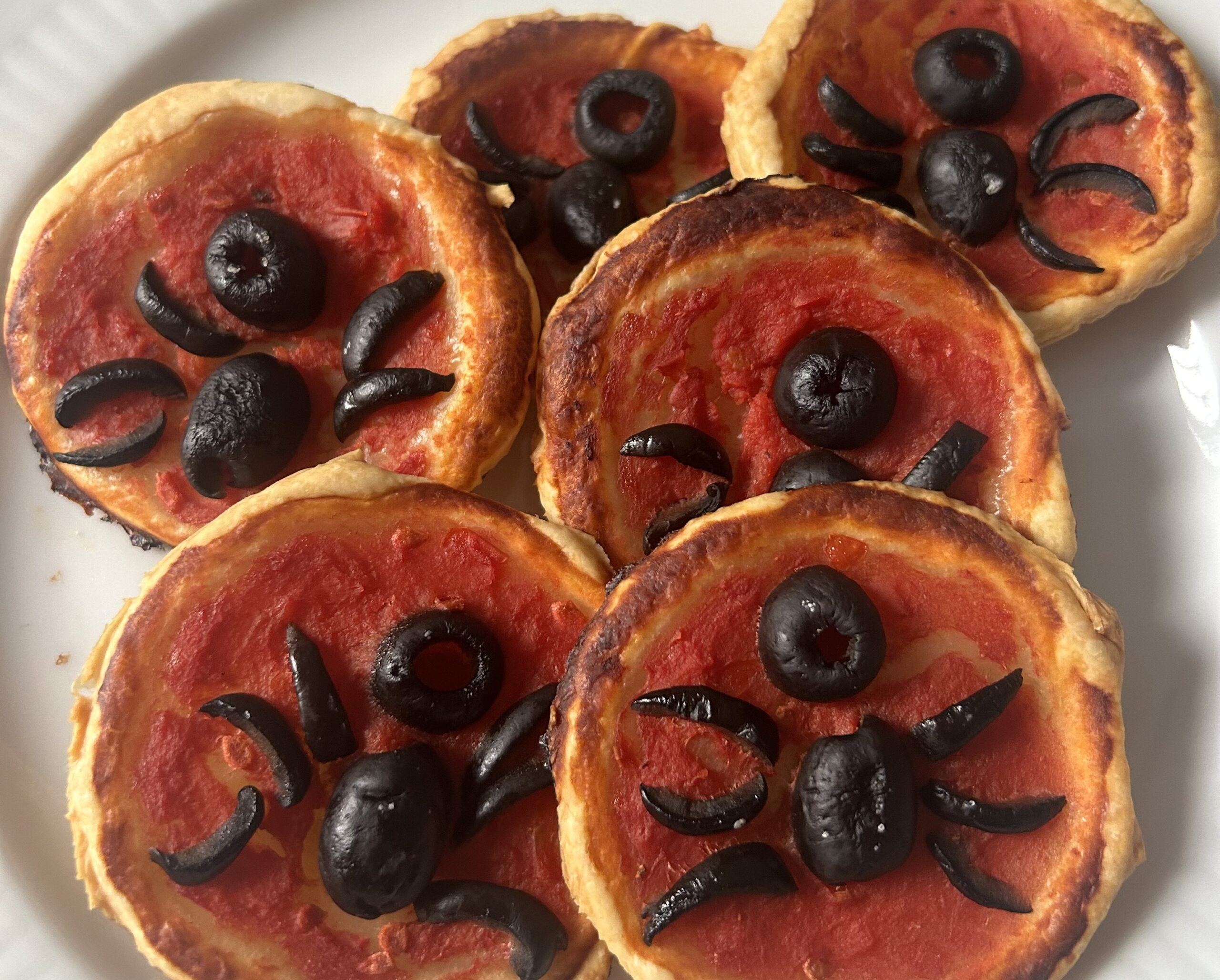 Pizzette con decorazione a forma di ragno fatta di olive nere. Pizzette senza formaggio