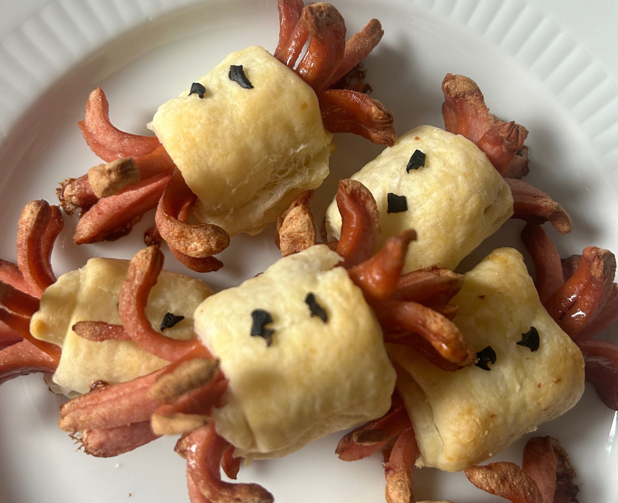 Snack di würstel per Halloween avvolti in pasta sfoglia, per feste e aperitivi. I würstel sono tagliati e incisi per creare divertenti tentacoli che si arricciano durante la cottura, mentre la pasta sfoglia dorata li avvolge al centro. Decorati con pezzetti di olive nere, questi finger food assumono un aspetto giocoso, ideali per buffet o eventi informali. Scopri come preparare questo stuzzichino sfizioso e originale in pochi semplici passi