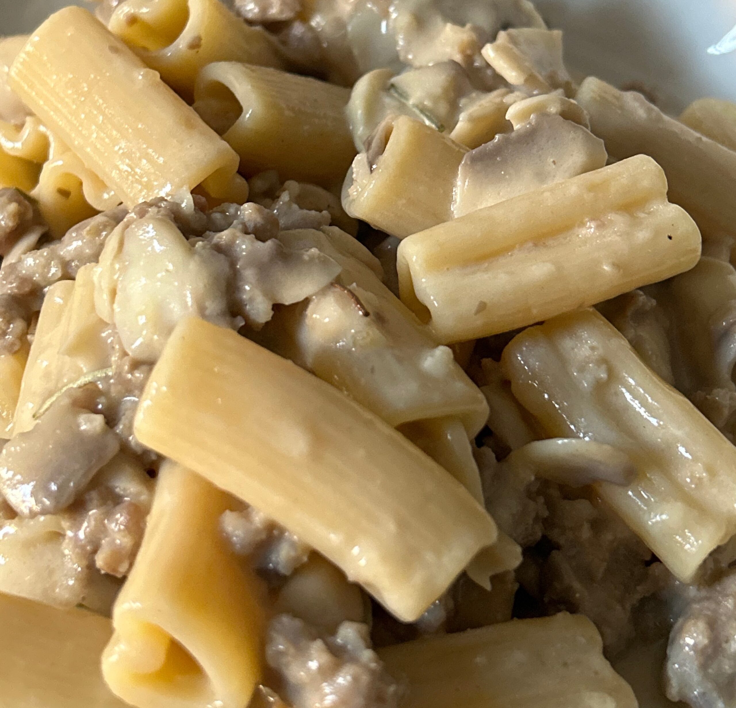 Piatto di pasta cremosa con salsiccia e funghi champignon