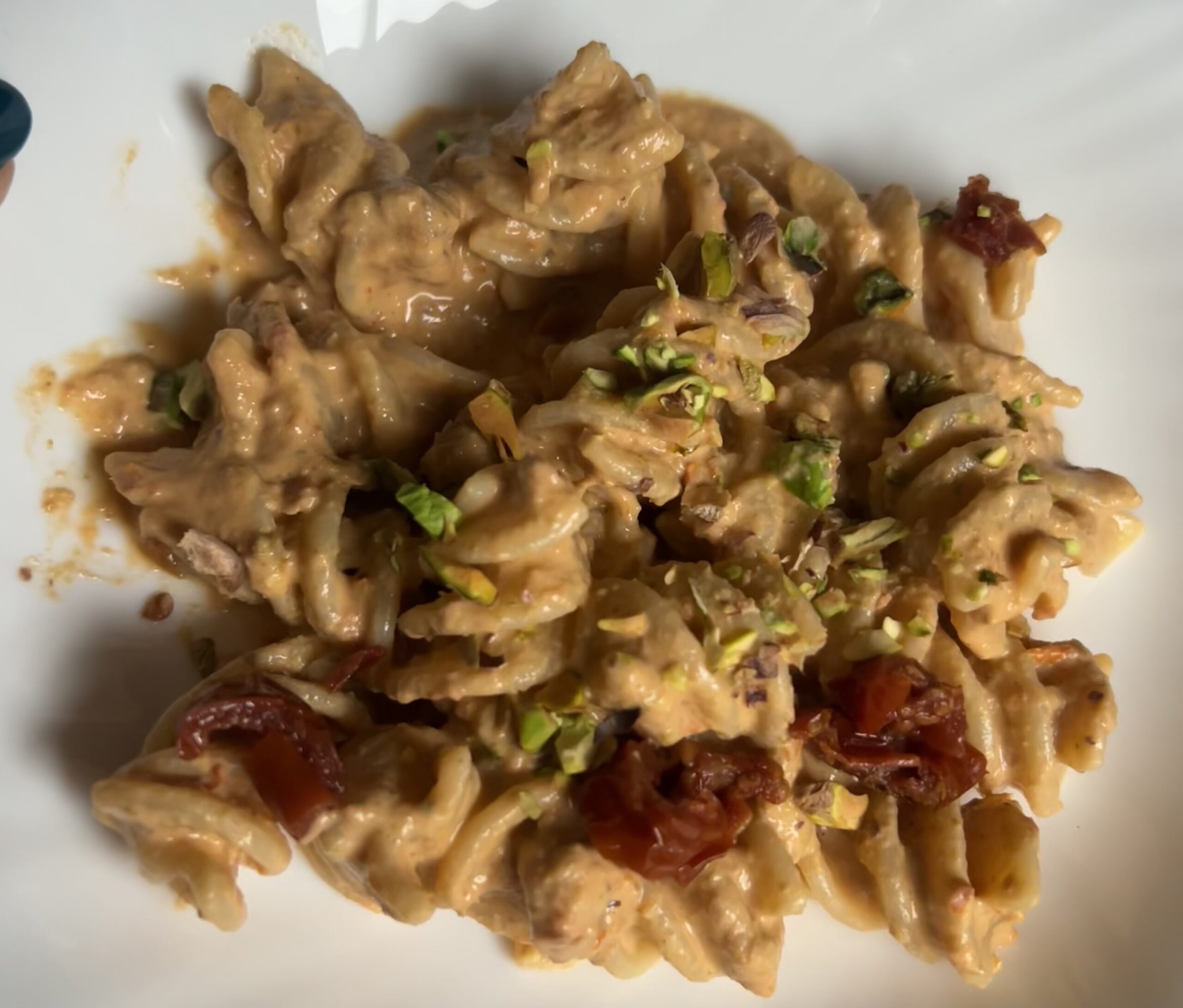 Pasta con sugo di pistacchi, robiola e pomodorini secchi. Fusilloni su un piatto, con un sugo cremoso guarniti con granella di pistacchio e pezzi di pomodorini secchi.